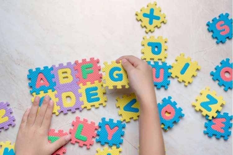 Crianças brincando com alfabeto de EVA em forma de quebra-cabeça.