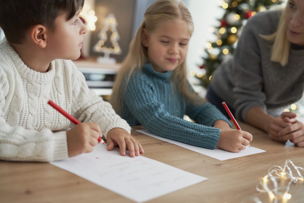 Um menino e uma menina crianças escrevendo em papéis com ajuda de um adulto.