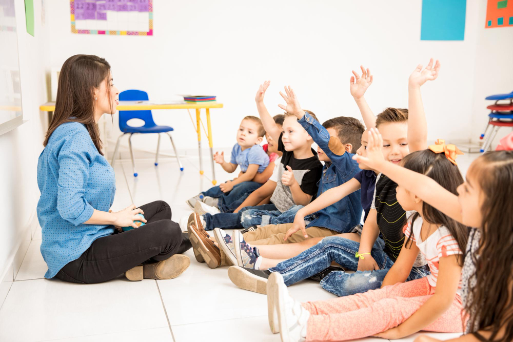 Professora do Ministério Infantil sentada à frente da sala com várias crianças com a mão erguida.