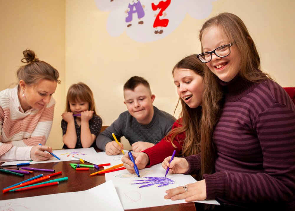 Crianças com deficiência participando de atividade artística com professora, representando inclusão no Ministério Infantil e valorização da diversidade.