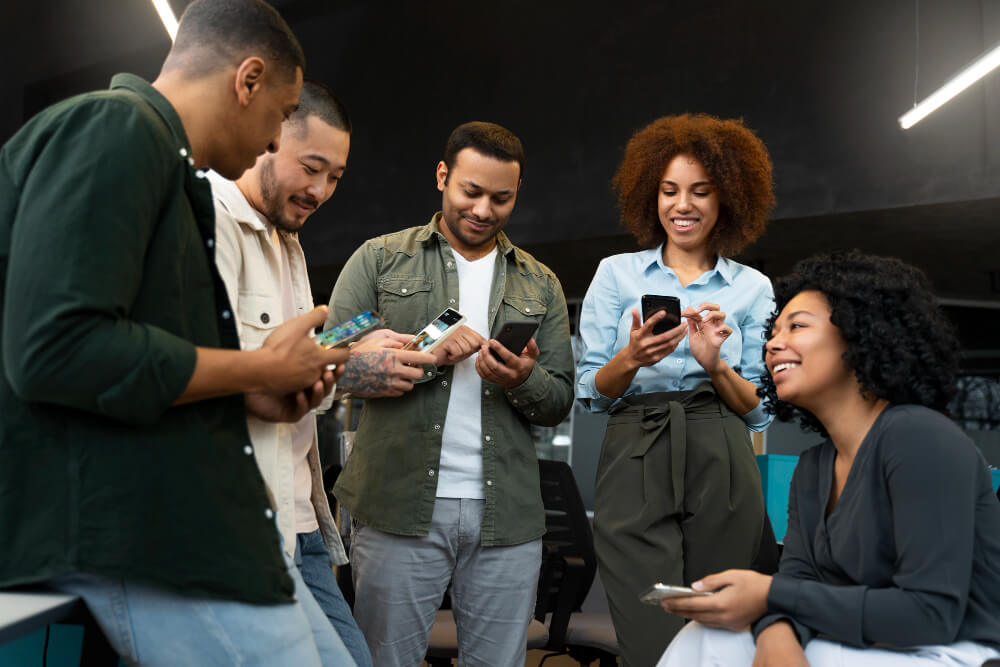 Grupo de profissionais reunidos em escritório utilizando smartphones, representando o uso de tecnologia para empresas em ambientes corporativos.