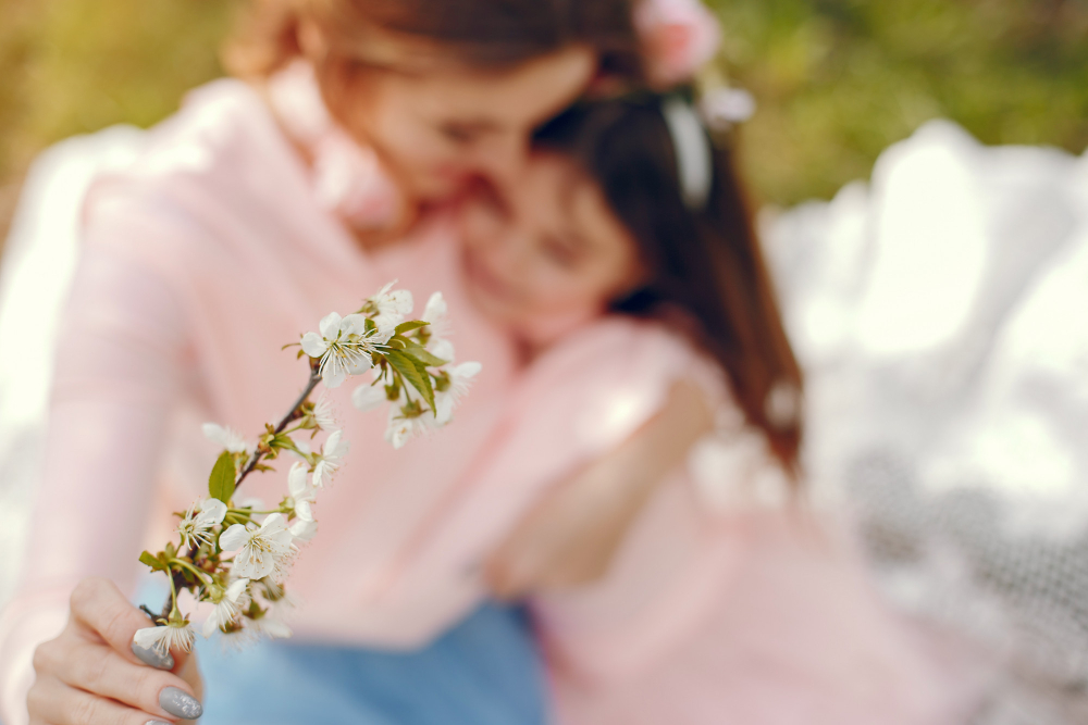 Mãe e filha em momento de carinho ao ar livre com flores, representando o amor celebrado no Dia das mães na igreja
